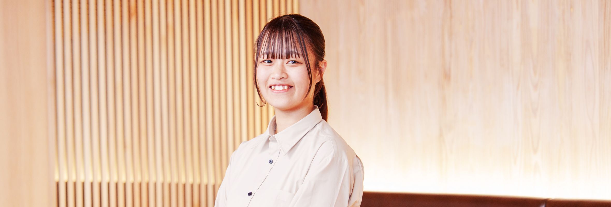 S.K.さんの正面写真。象牙色の生地に黒色のボタンが付いたワイシャツを身に付けている。