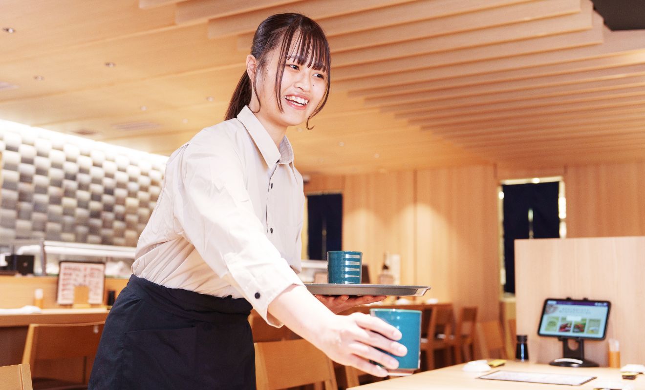 S.K.さんが、お茶が入った湯呑みを、テーブル席に置こうとしている様子。