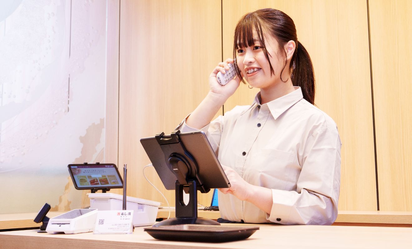 S.K.さんが予約の受付をしている様子。右手に持った受話器を耳に当て、左手でタッチパッドを操作している。